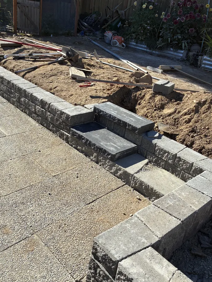 Paver patio project during construction showing the capped segmental retaining wall and integrated steps